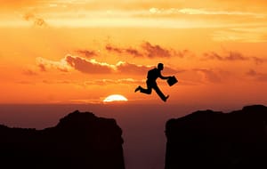persoon springt over een klif tegen een achtergrond van de ondergaande zon